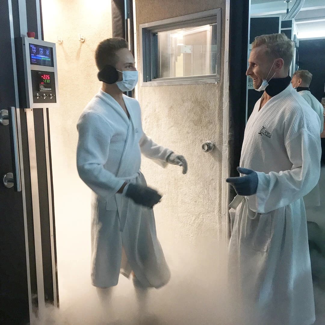 Jordan and Steve in white robes beside an open cryotherapy chamber.