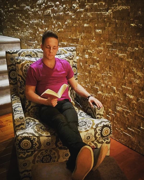 Jordan reading in a patterned armchair beside a stone wall.