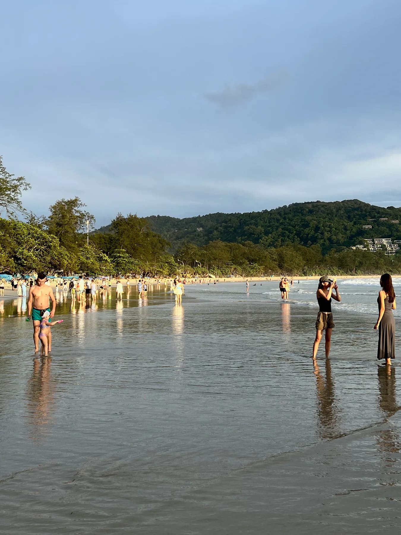 People standing along the water at Kata Beach in the evening light.