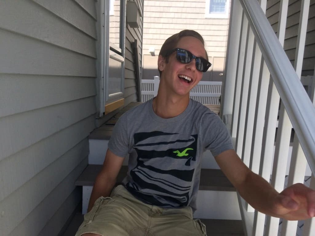 Jordan laughing in sunglasses while seated on outdoor steps.